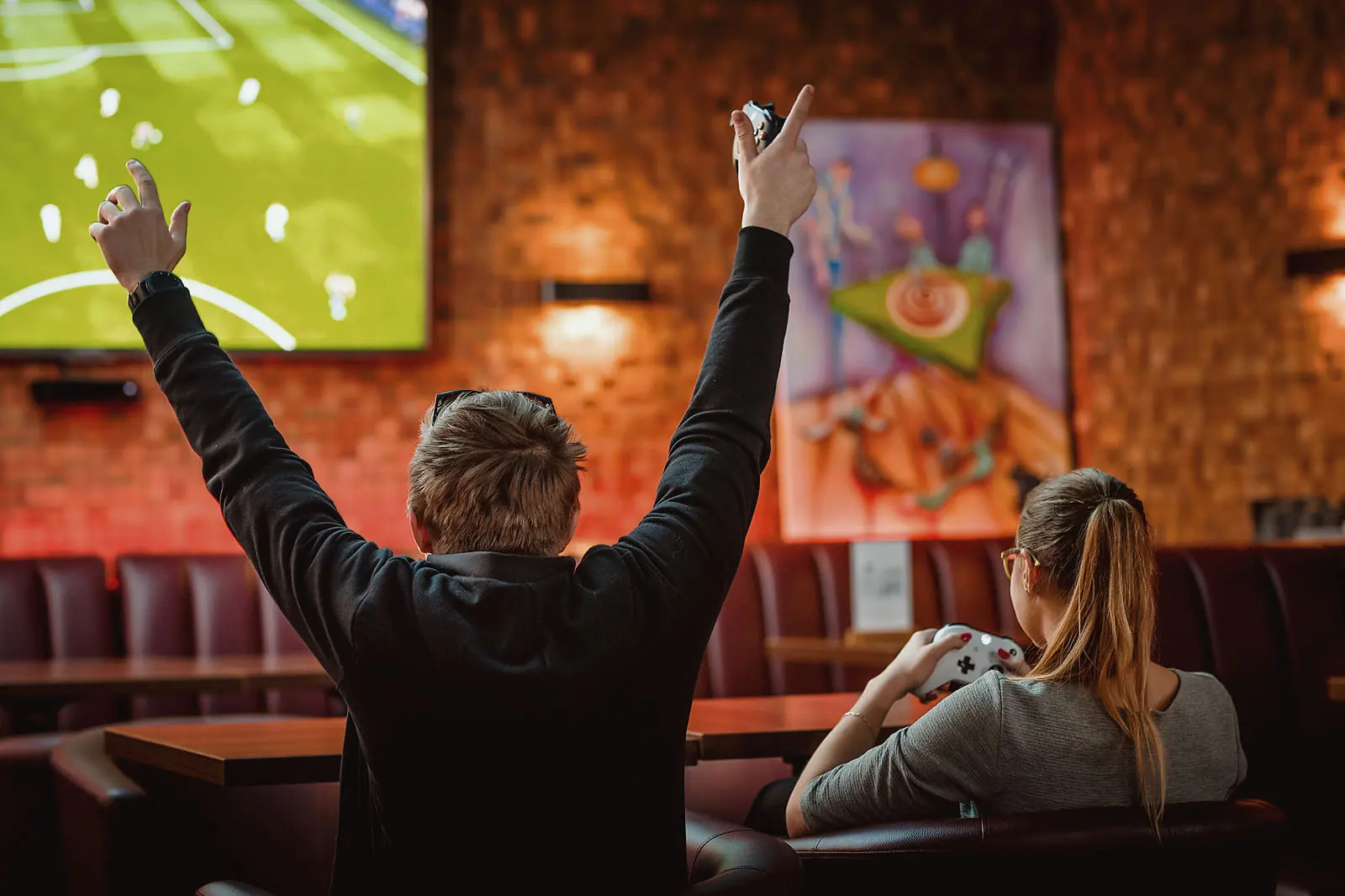 Gość cieszy się przed ekranem, obok gościni z padem od Xboxa