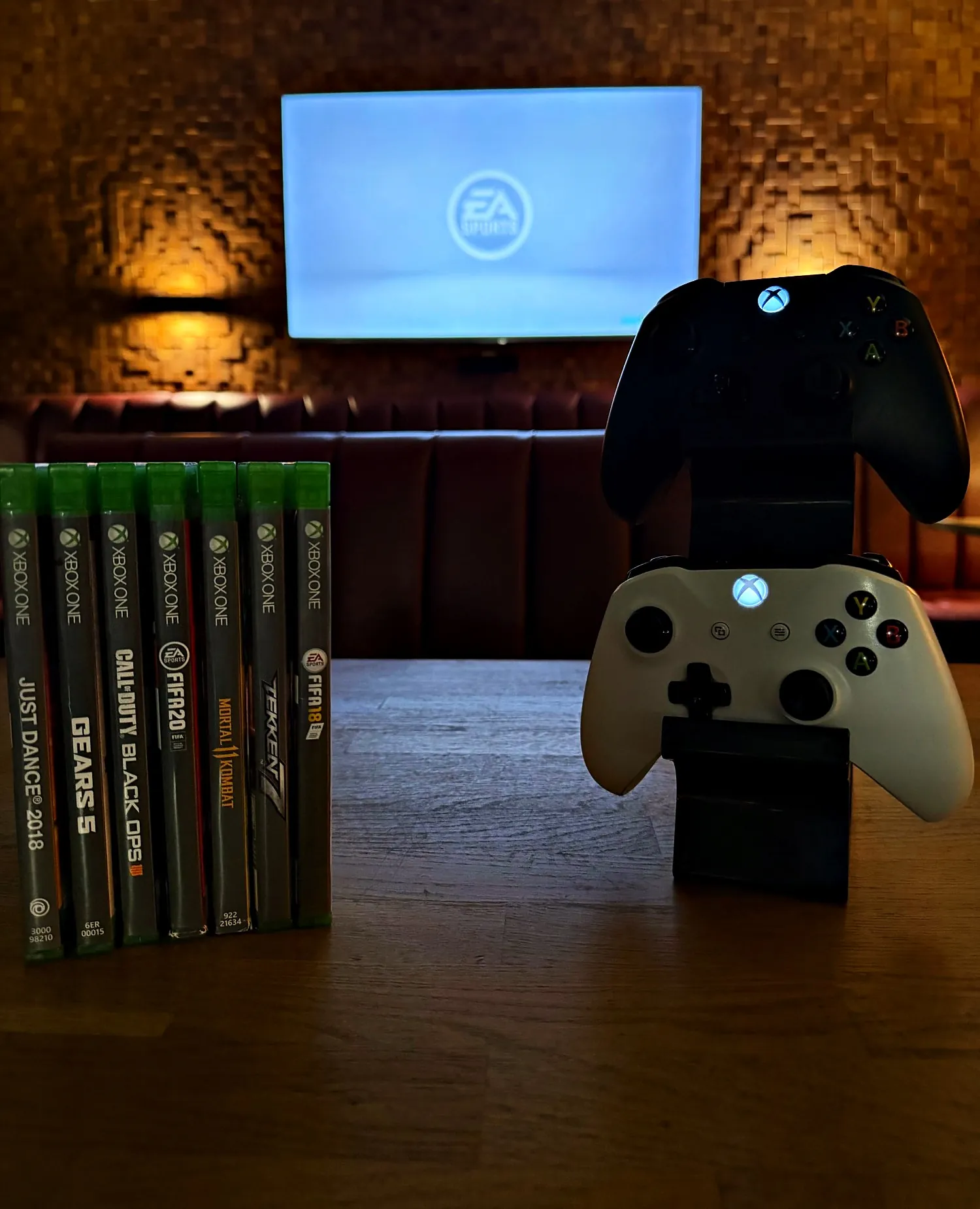 Dwa pady do Xboxa i gry na Xbox One na stoliku przed ekranem w Klubie Pictures